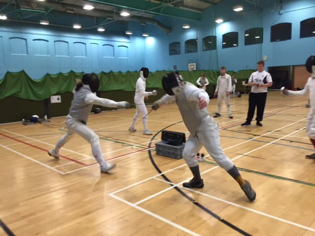 A fencing bout watched by a referee and other competitors