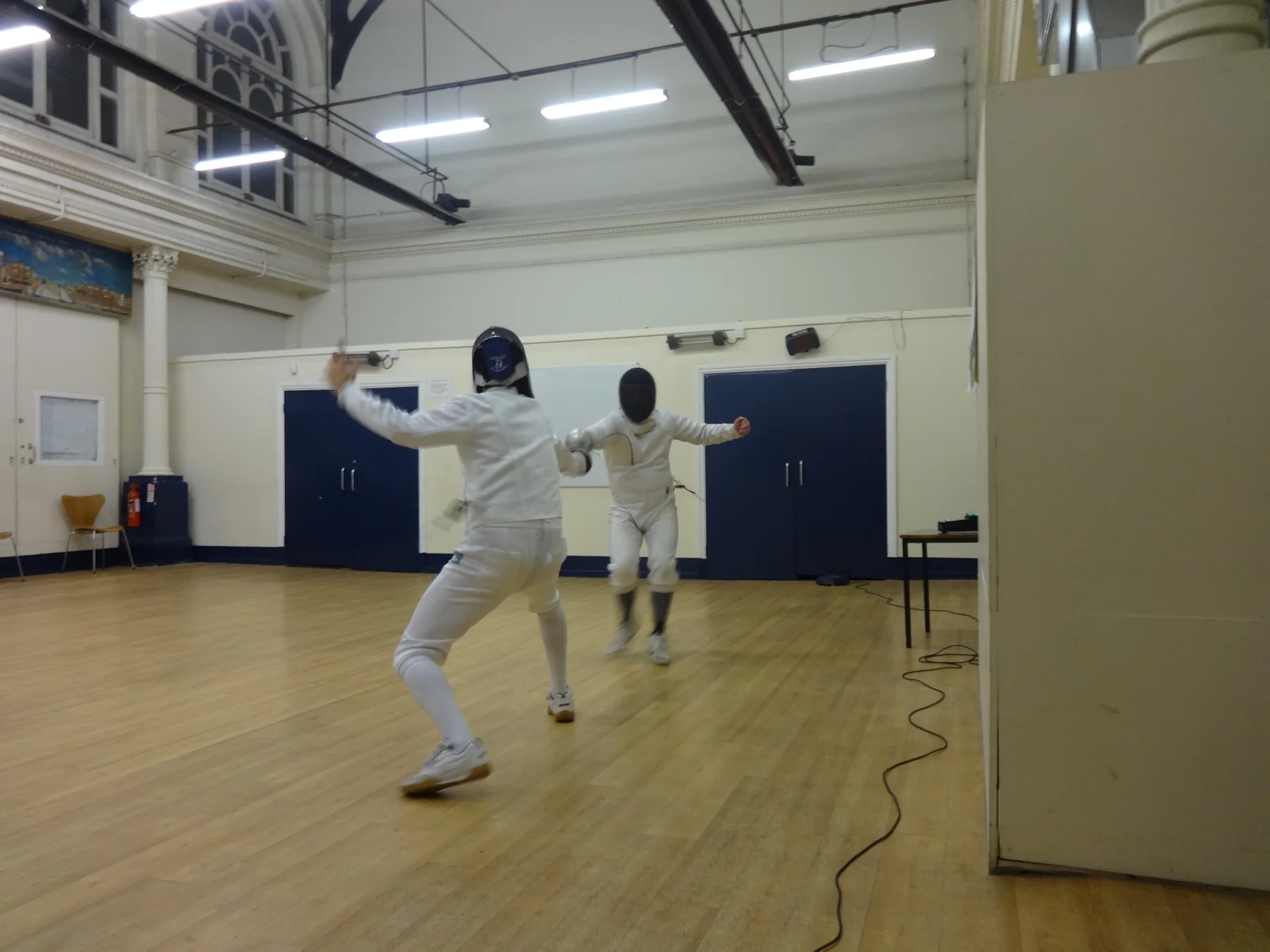 Two foil fencers practising footwork in the club hall